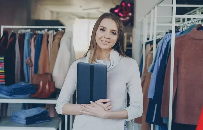 Smiling shop owner standing in a clothing boutique holding a digital tablet, representing local retail and services